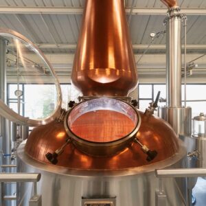 A copper distillery tank, with the glass door open to see inside of the tank.